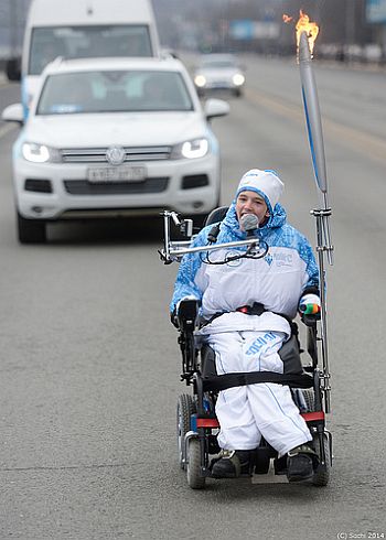 Osoba na wózku elektrycznym z pochodnią paraolimpijską
